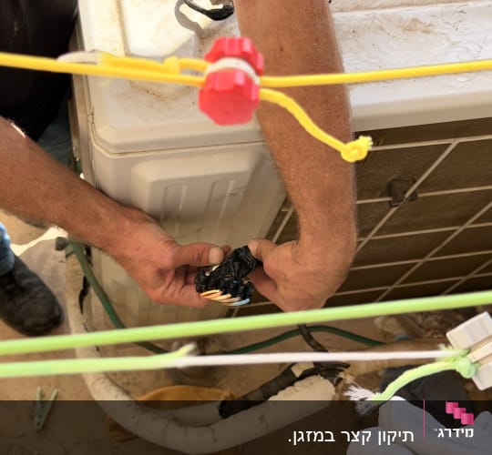 טכנאי מזגנים מתקן רכיבי חשמל וחיווט ביחידה החיצונית של המזגן